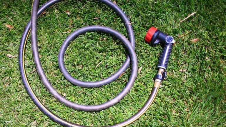 Coiled garden hose with spray nozzle attachment lying on green grass lawn in circular loops