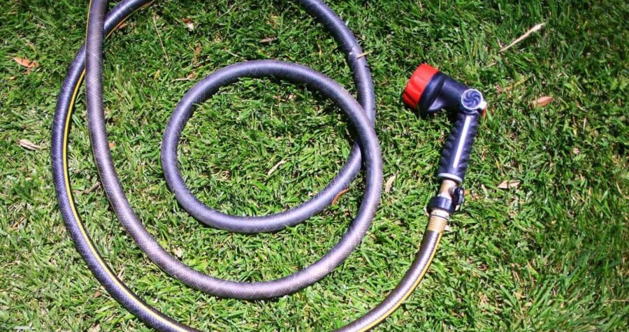 Coiled garden hose with spray nozzle attachment lying on green grass lawn in circular loops