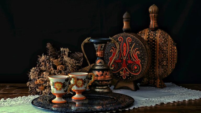 Collection of ornate decorative objects including painted teacups, ornamental bottles, circular platter, and dried flowers arranged on wooden surface