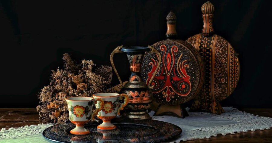 Collection of ornate decorative objects including painted teacups, ornamental bottles, circular platter, and dried flowers arranged on wooden surface