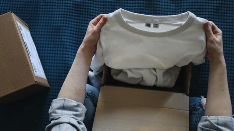 Person holding a white T-shirt over an open cardboard box