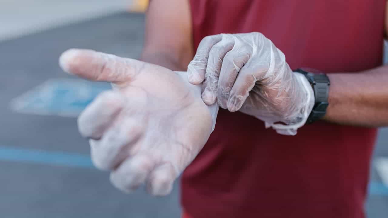 Person wearing a red shirt putting on a transparent disposable glove outdoors