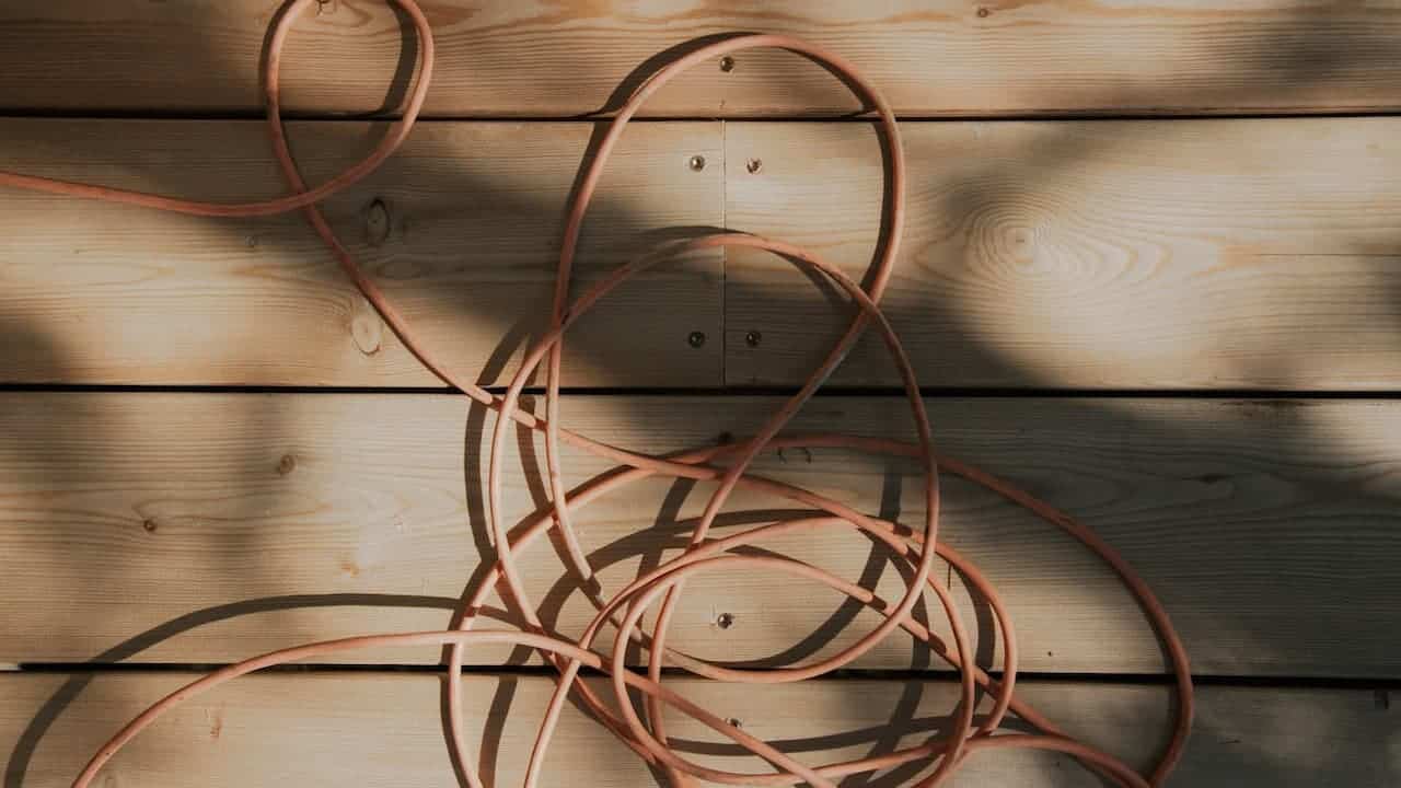 Tangled copper or orange-colored wire cables coiled and twisted together against a wooden plank wall background