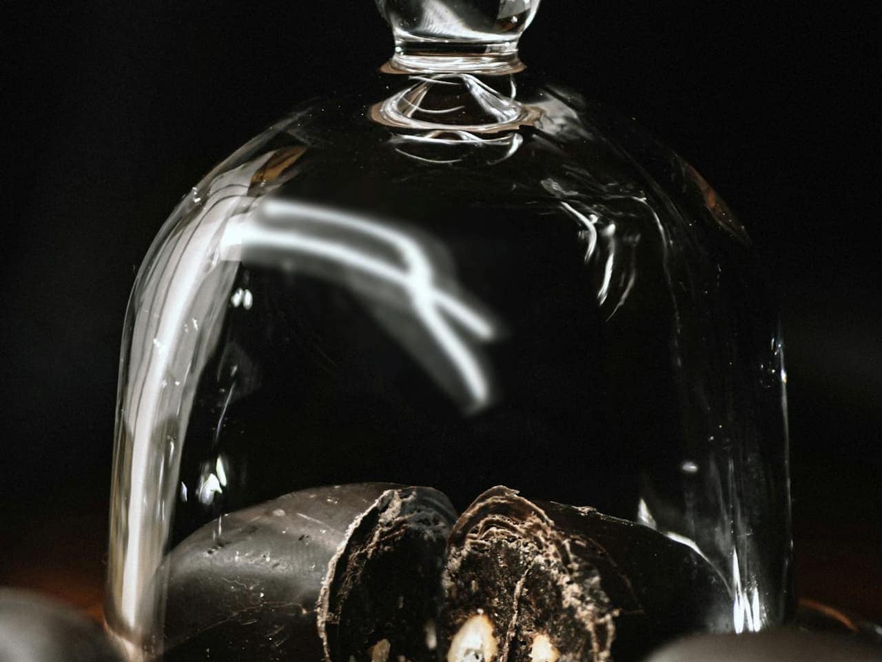 Glass cloche cover placed over a black cake on a serving stand, showcasing the dessert while keeping it protected