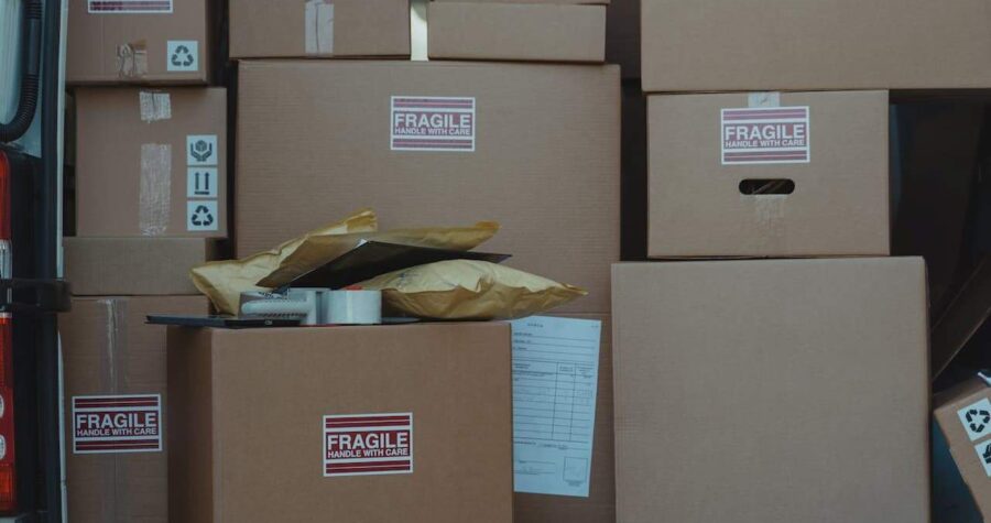Stacked cardboard moving boxes labeled "FRAGILE HANDLE WITH CARE" with packing materials and documents scattered around