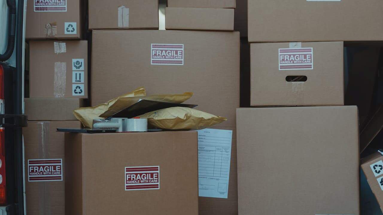 Stacked cardboard moving boxes labeled "FRAGILE HANDLE WITH CARE" with packing materials and documents scattered around