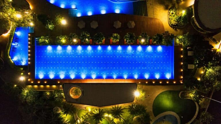 Aerial night view of an illuminated swimming pool surrounded by greenery and lights