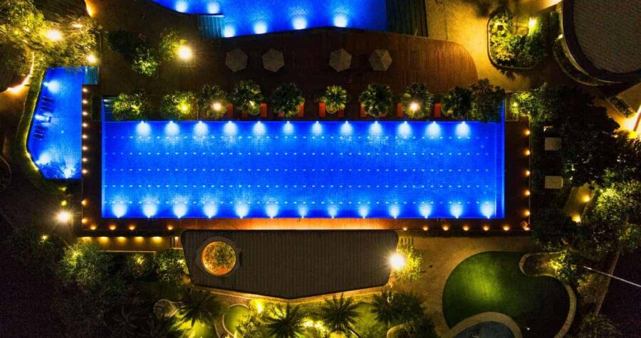 Aerial night view of an illuminated swimming pool surrounded by greenery and lights