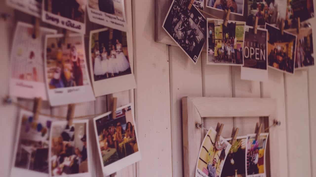 Personal photographs and postcards pinned to white wooden wall panels with clothespins, creating informal memory display