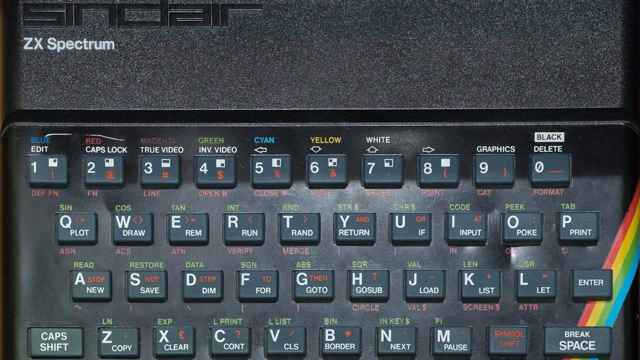 Sinclair ZX Spectrum computer keyboard with black keys, colored text labels, and rainbow stripe logo on right side