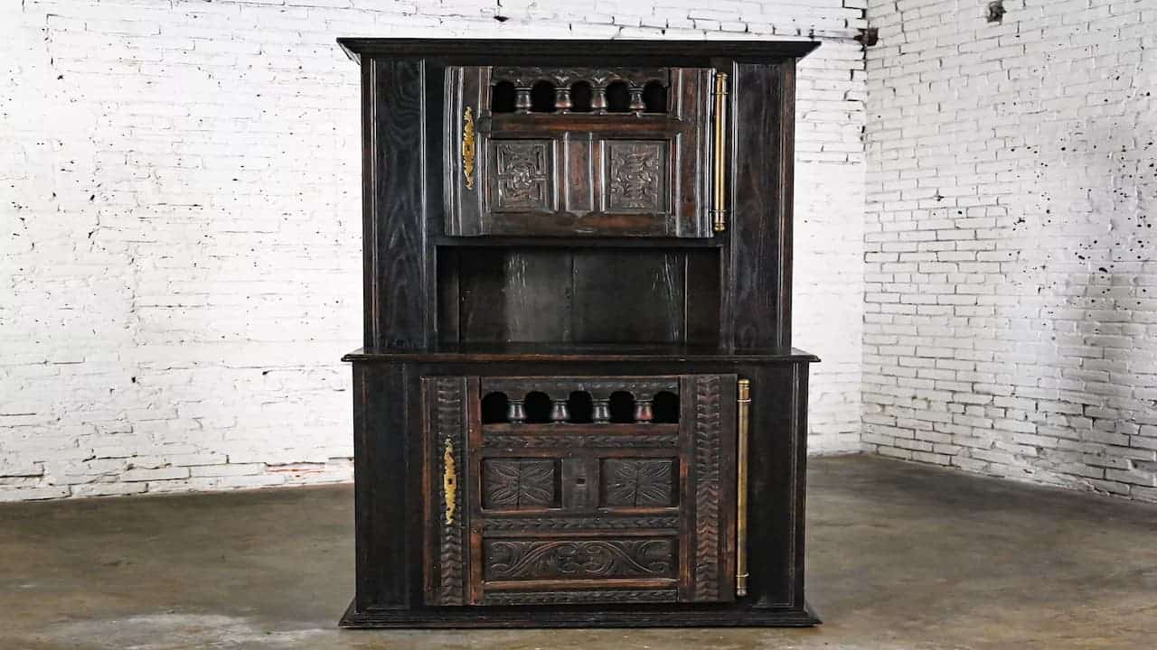 Dark wooden Colonial Revival oak cabinet with carved decorative panels, open shelving, and ornate details against white brick wall