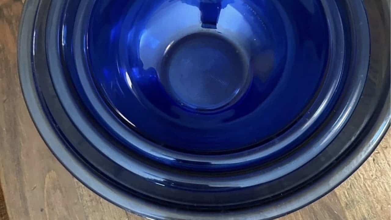 Stack of nested blue glass Pyrex mixing bowls of varying sizes on wooden surface showing concentric circular pattern