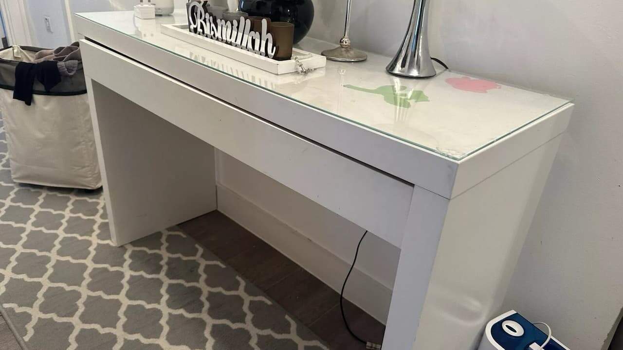 White glass-top console table with decor items on top, placed on a patterned grey rug