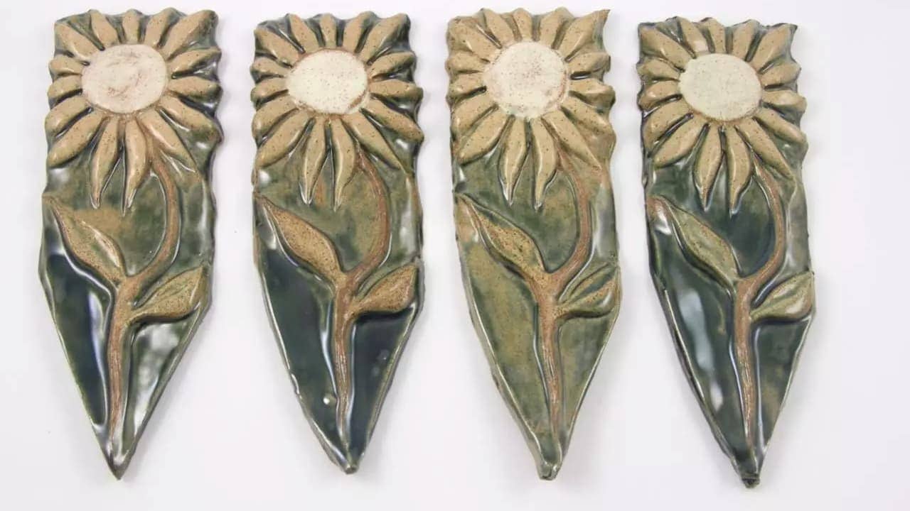 Four hand-painted ceramic garden markers in teardrop shape featuring raised sunflower designs with green glaze and brown accents
