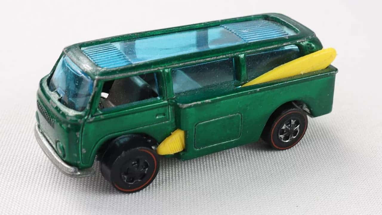 Green Hot Wheels diecast toy van with a blue-tinted roof and windshield, yellow surfboards mounted on the side, and black wheels with red accents
