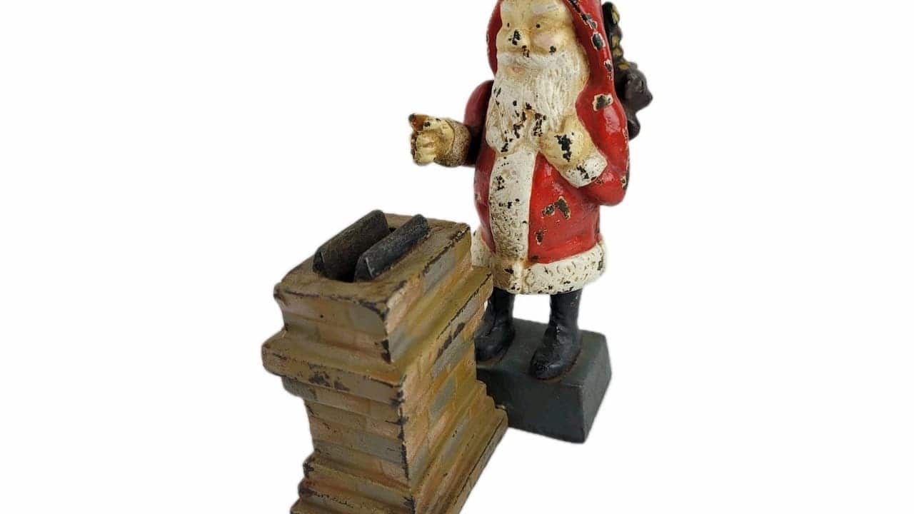 Vintage painted cast iron Santa Claus figurine standing beside a chimney, with visible wear and chipping on the red and white paint