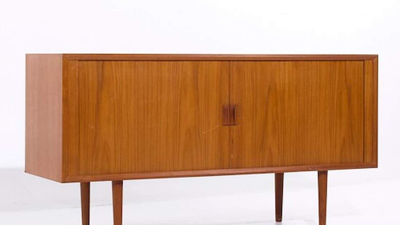 Mid-century modern teak credenza with sliding doors, wooden handles, and tapered legs on white background