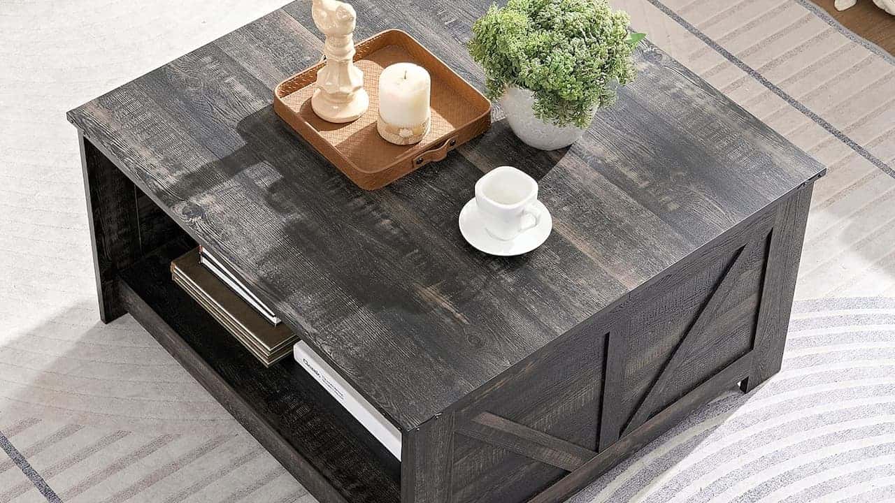 Dark wood coffee table with white coffee cup, wooden tray with candles, and gray upholstered furniture in background