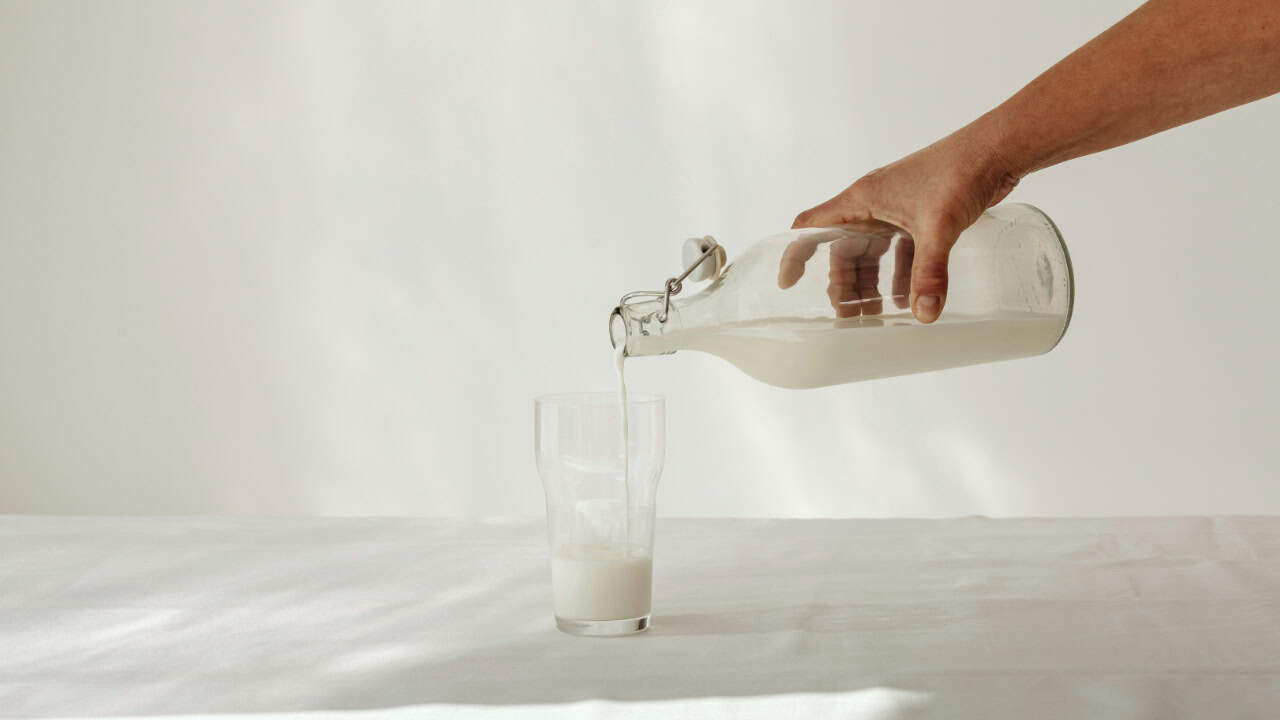 A person pouring milk into a glass on a table