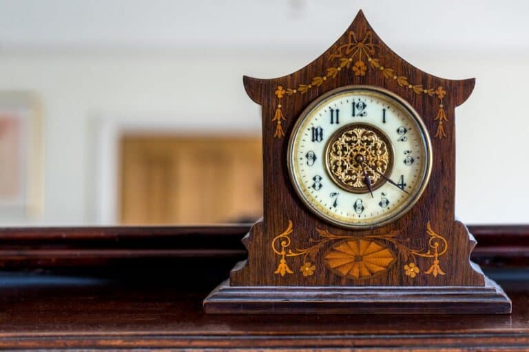 Antique wooden mantel clock, floral inlay design, round white clock face with Roman numerals, placed on polished wood surface