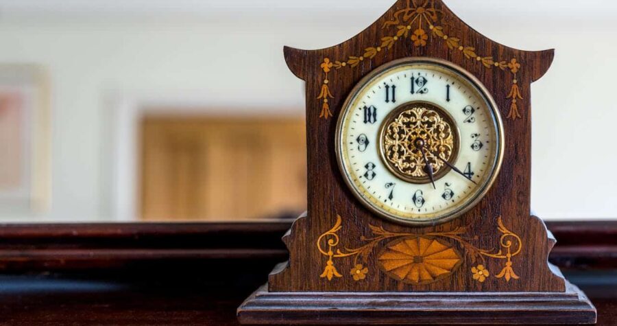 Antique wooden mantel clock, floral inlay design, round white clock face with Roman numerals, placed on polished wood surface