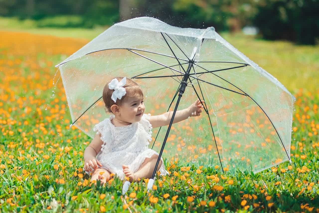 Adorable Baby with Umbrella in Blooming Field