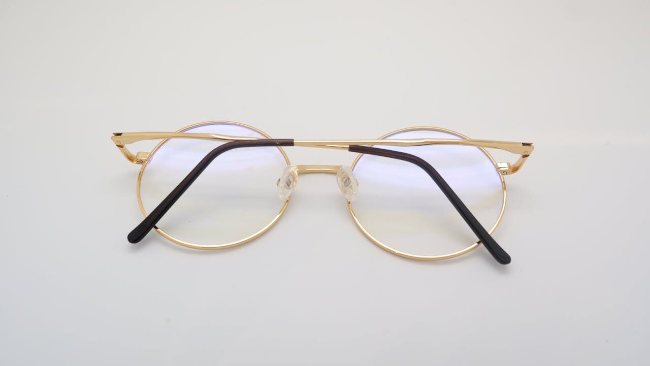 Round gold-rimmed prescription glasses with black temple tips, placed on a white surface