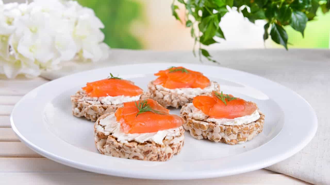 Plate with four round crispbread canapés, each topped with cream cheese, smoked salmon slices, and a sprig of dill, arranged neatly on a white plate