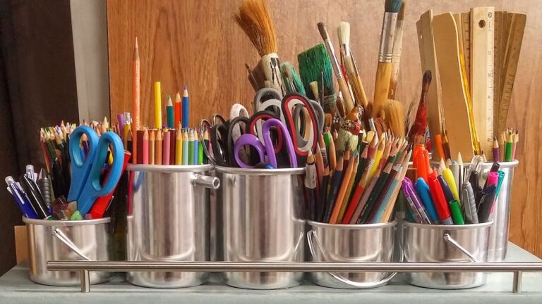 Metal containers filled with colored pencils, scissors, paintbrushes, rulers, pens, markers, organized neatly on a shelf