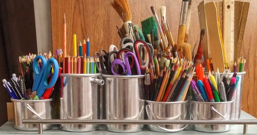 Metal containers filled with colored pencils, scissors, paintbrushes, rulers, pens, markers, organized neatly on a shelf