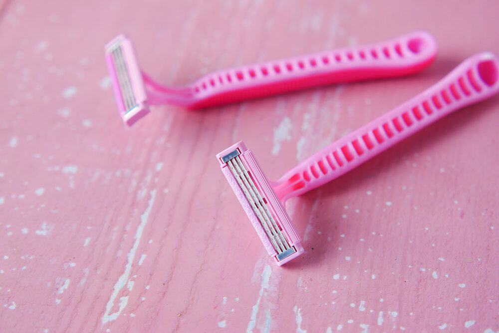 Two pink disposable razors with multi-blade heads, placed on a distressed pink wooden surface, personal grooming items