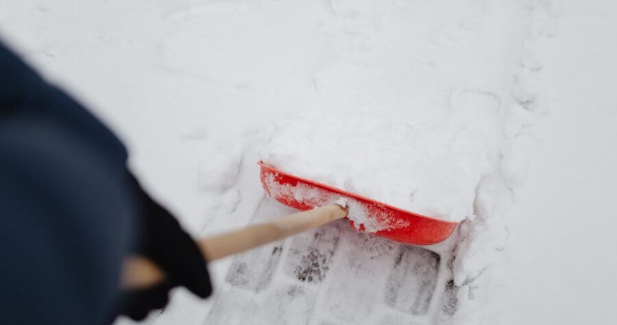 Person Holding Red and Brown Shovel on Snow Covered Ground