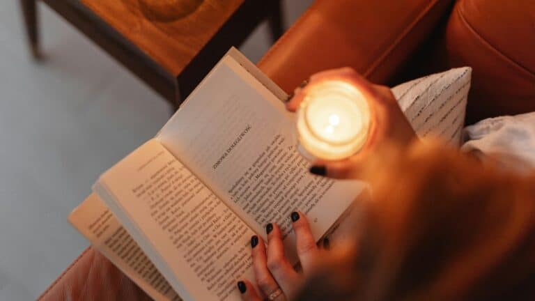 Woman sitting on a couch reading a book with a candle