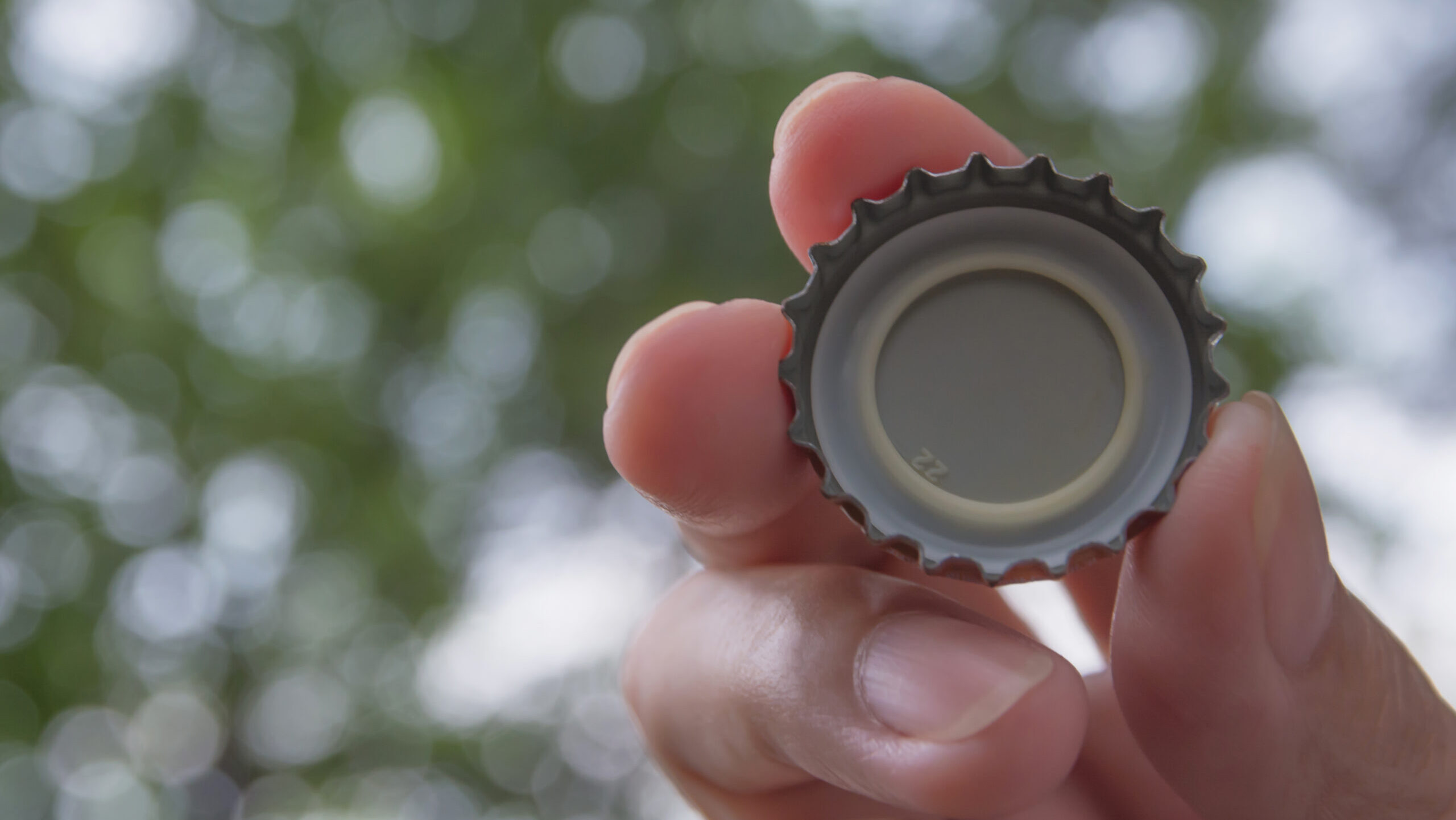 Hand holding a bottle caps on nature background.